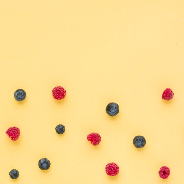 An elevated view of raspberries and blueberries on yellow background