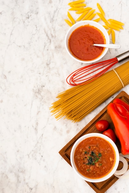 Free photo elevated view of raw pasta and tomato sauce on marble textured background