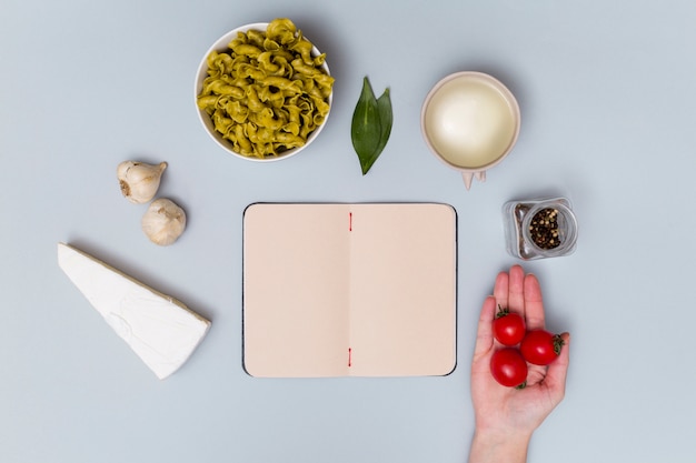 Free Photo elevated view of red cherry tomato with pasta ingredient and open notebook