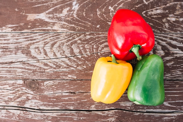 Free photo an elevated view of red; yellow and green bell peppers on an old wooden desk