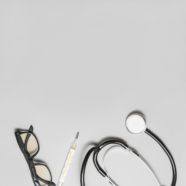 Free photo elevated view of spectacles; stethoscope and thermometer on grey background