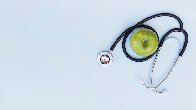 An elevated view of stethoscope around the green apple over blue background