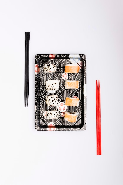 An elevated view of sushi with juicy salmon fish on tray near chopsticks isolated over white surface