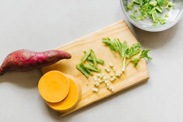 Elevated view of sweet potato; sliced pumpkin and celery on cutting board