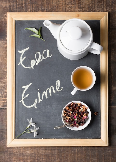 Free photo an elevated view of teapot; lime tea cup and dried herbs with leaves and flower on slate