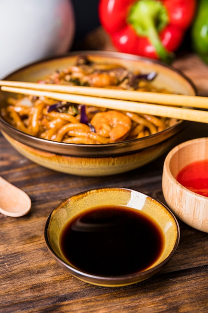 An elevated view of thai udon noodle with chopsticks and soya sauce on wooden table