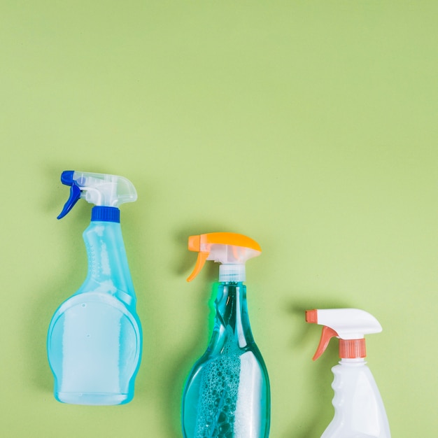 Elevated view of three spray bottles on green background