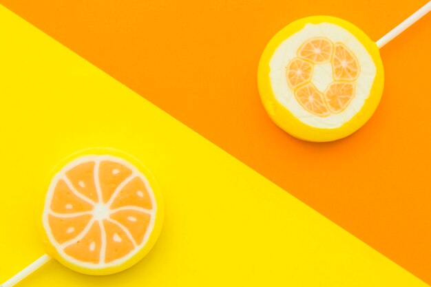 Elevated view of two citrus fruit lollipops opposite each other on multi colored background