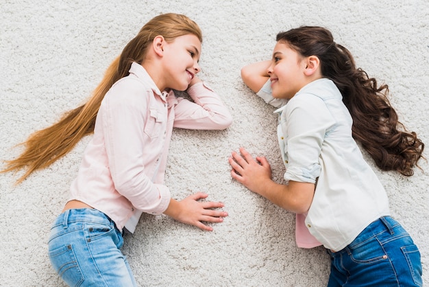 Free photo an elevated view of two smiling girls lying on carpet looking at each other