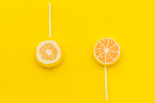 Elevated view of two sweet citrus lollipops on yellow surface