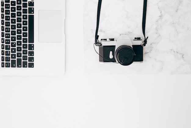 An elevated view of vintage camera and laptop on white desk