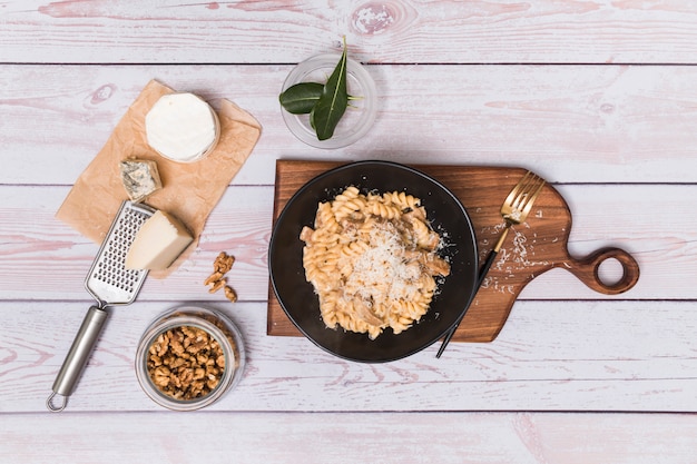 Free photo elevated view of walnut and delicious twisted fusilli pasta garnish with grate cheese on wooden surface