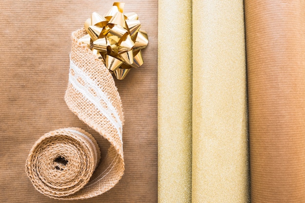 Free photo elevated view of weaving ribbon and golden bow with gift paper on brown paper