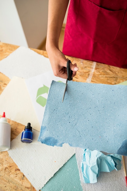 Elevated view of woman's hand cutting blue paper with scissors