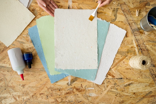 Free photo elevated view of a woman's hand using paintbrush over handmade papers