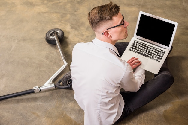 Free Photo an elevated view of young man holding laptop in hand sitting on floor