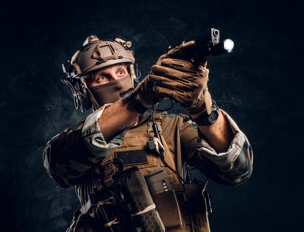 Free photo elite unit, special forces soldier in camouflage uniform holding a gun with a flashlight and laims at the target. studio photo against a dark textured wall