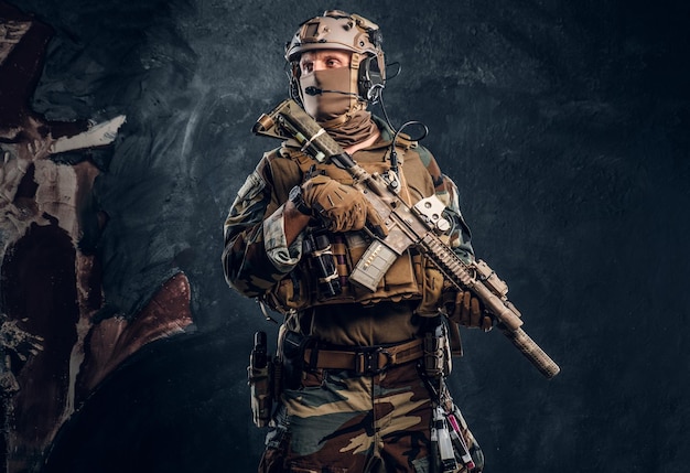 Elite unit, special forces soldier in camouflage uniform posing with assault rifle. Studio photo against a dark textured wall