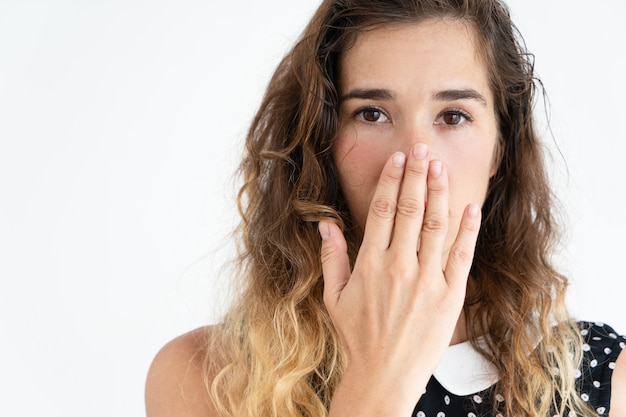 Embarrassed young pretty woman covering mouth with hand and looking at camera.