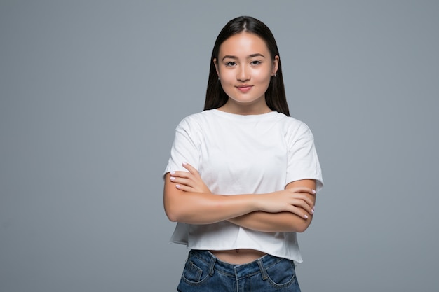 Emotion concept. Portrait of angry cute asian woman standing posing with crossed arms looking at camera with grey clothes on a white background