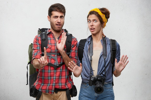 emotional bearded guy and beautiful woman with professional camera gesturing with both hands, making stop sign, expressing denial, reject, unwillingness. Human emotions and feelings