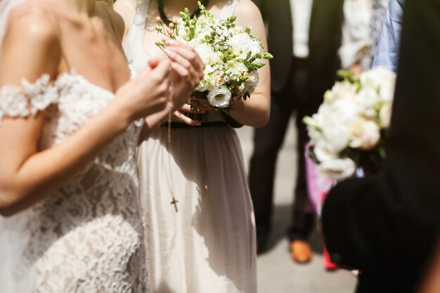 Emotional beautiful brunette bride in white vintage dress putting on crucifix