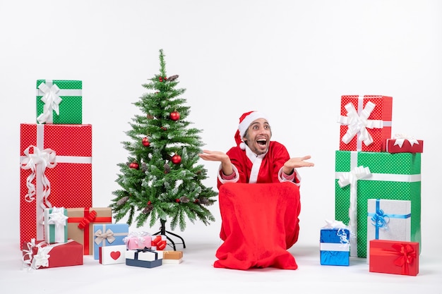 Free Photo emotional excited young man dressed as santa claus with gifts and decorated christmas tree reacts happily on white background