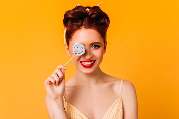 Emotional ginger girl holding lollipop and smiling. Front view of european woman with hard candy.