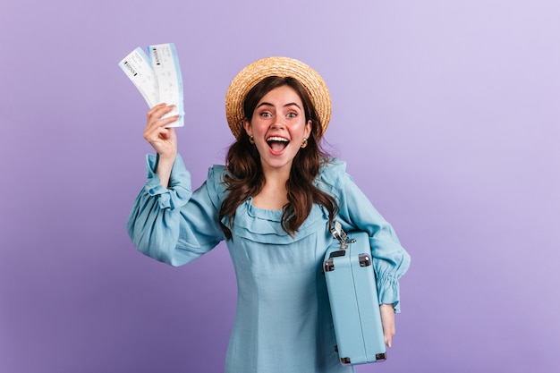 Free photo emotional girl excitedly shows tickets for plane and retro luggage. woman rejoices on upcoming journey.