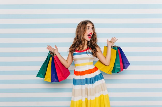 Emotional girl is shocked by big discounts during black friday and buys lot of clothes. Full-length portrait of  woman in bright dress with shopping bags