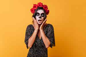 Free photo emotional mexican dark-haired woman with flowers on her head makes shocked face touching herself with her hands