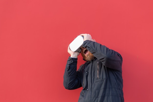 Emotional portrait of a man on the street wearing reality glasses against the background of a red wall