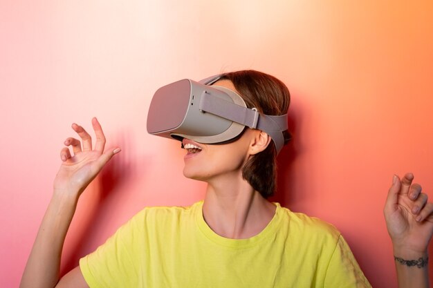 Emotional portrait of woman in virtual reality glasses in studio on pink orange background