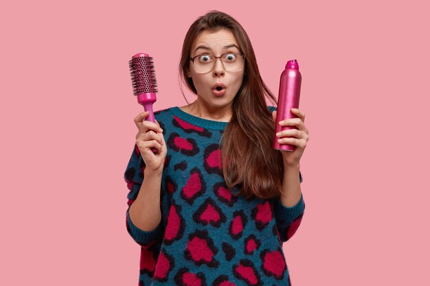 Emotional stupefied emotive woman in beauty salon, surprised by new hairstyle, stares with widen eyes, dressed in sweater with pink stains