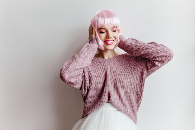 Free photo emotional trendy girl with shiny pink hair standing in front of white wall. indoor photo of carefree lady in peruke and oversize purple sweater.