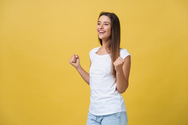 Emotions, expressions, success and people concept - happy young woman or teenage girl celebrating victory isolated over yellow background.