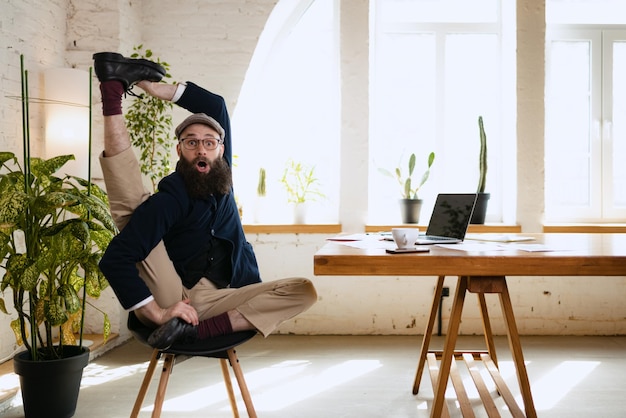 Free photo emotive man stretching his leg at office while working on laptop businessman resting