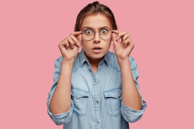 Emotive young Caucasian woman stares though big eyewear