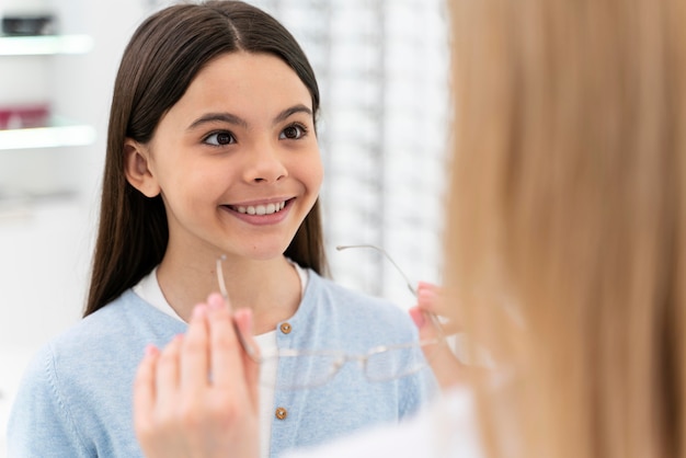 Employee helping girl to try on glasses