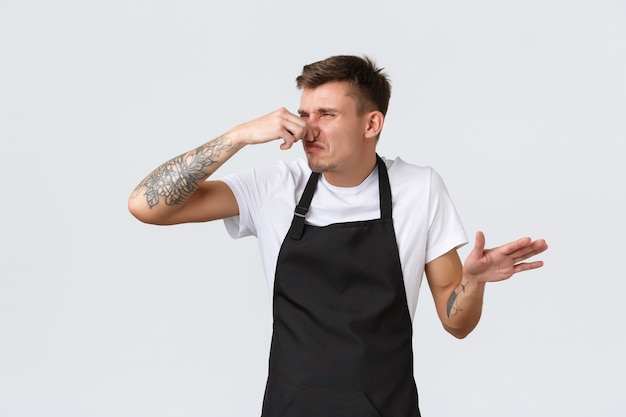 Employees, grocery stores and coffee shop concept. Annoyed and tired funny barista, cafe looking frustrated, shut nose from disgusting smell, puzzled what rotten in fridge, white background