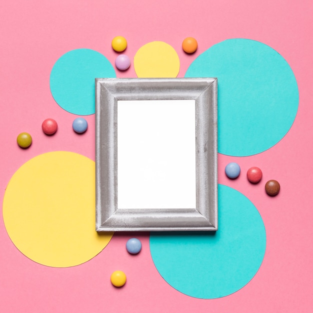 Free photo an empty blank frame with silver border on circular frame with colorful gems over the pink background