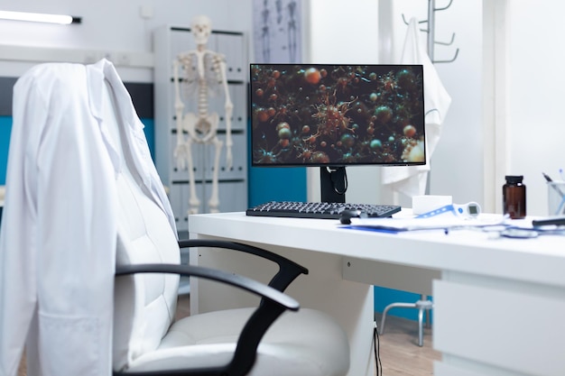 Empty bright medical office having computer on table with coronavirus cell on screen during virus examination. Hospital room with nobody in it equipped with professional tools. Virus illustration