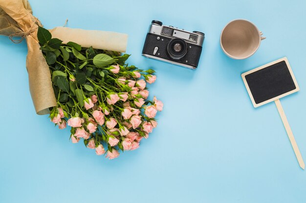 Empty cup; camera; pink roses bouquet and blank label on blue background