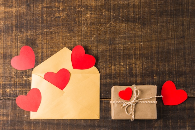 Empty envelope; hearts and gift box wrapped with brown paper arranged over textured surface