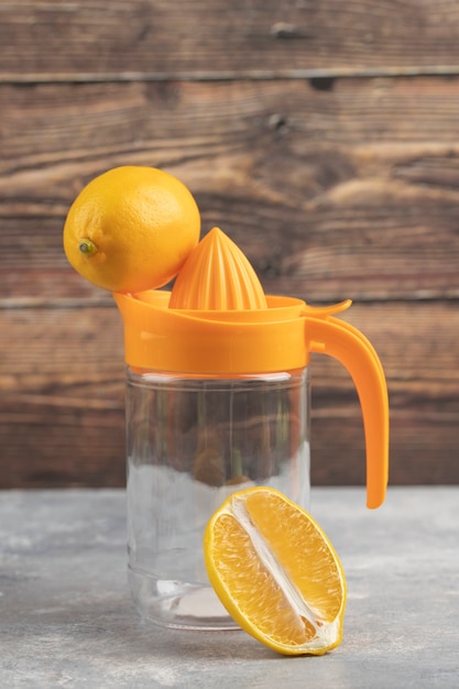 Free photo an empty glass pitcher with a one whole lemon on a wooden background.