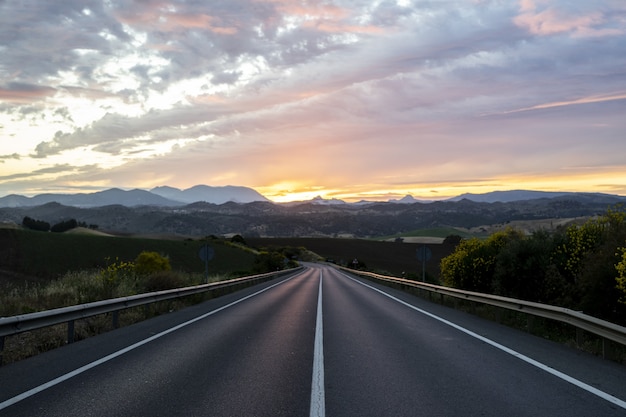 Free photo empty highway surrounded by hills under the cloudy sunset sky