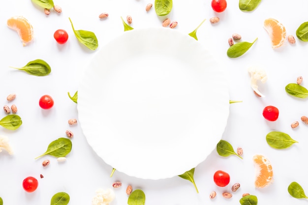 Free photo empty plate surrounded by pinto bean; vegetables and orange slices arranged on white background