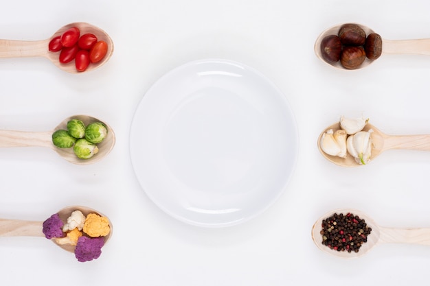 empty plate surrounded by vegetables in the wood spoons on white