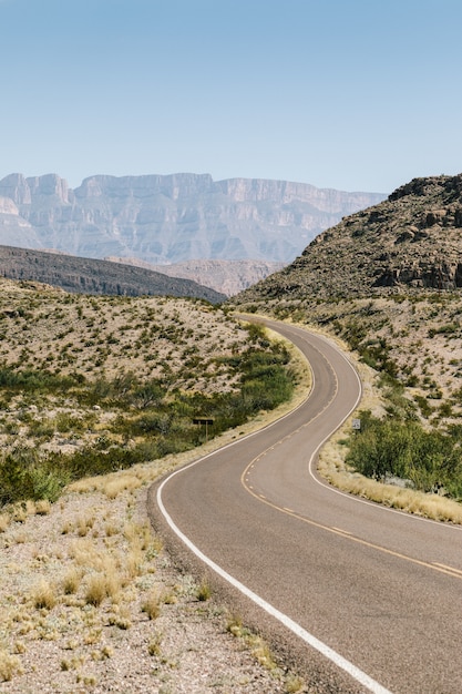 Free Photo empty road in the middle of a dry field with bushes and mountains in distance