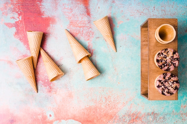 Empty waffle cones and chocolate ice cream in cups on multicolored background